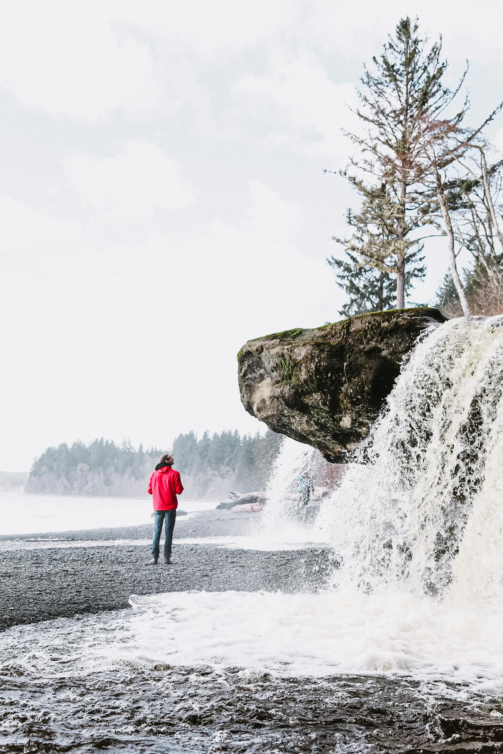 Man in red taking in the stunning Sandcut Beach waterfall in winter, BC.